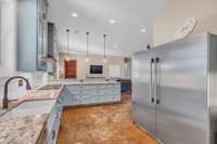 A bright farmhouse kitchen featuring light blue cabinets to the ceiling that add a soft, airy feel. The leathered granite countertops offer texture and warmth, complemented by sleek stainless steel appliances and under cabinet lighting.