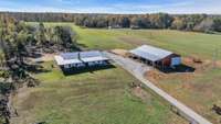 Aerial view of a 40-acre property in Springfield, TN featuring a modern farmhouse with rustic charm, surrounded by lush fields. Also with the property, a large 40x80 shop stands, offering ample space for work or storage.