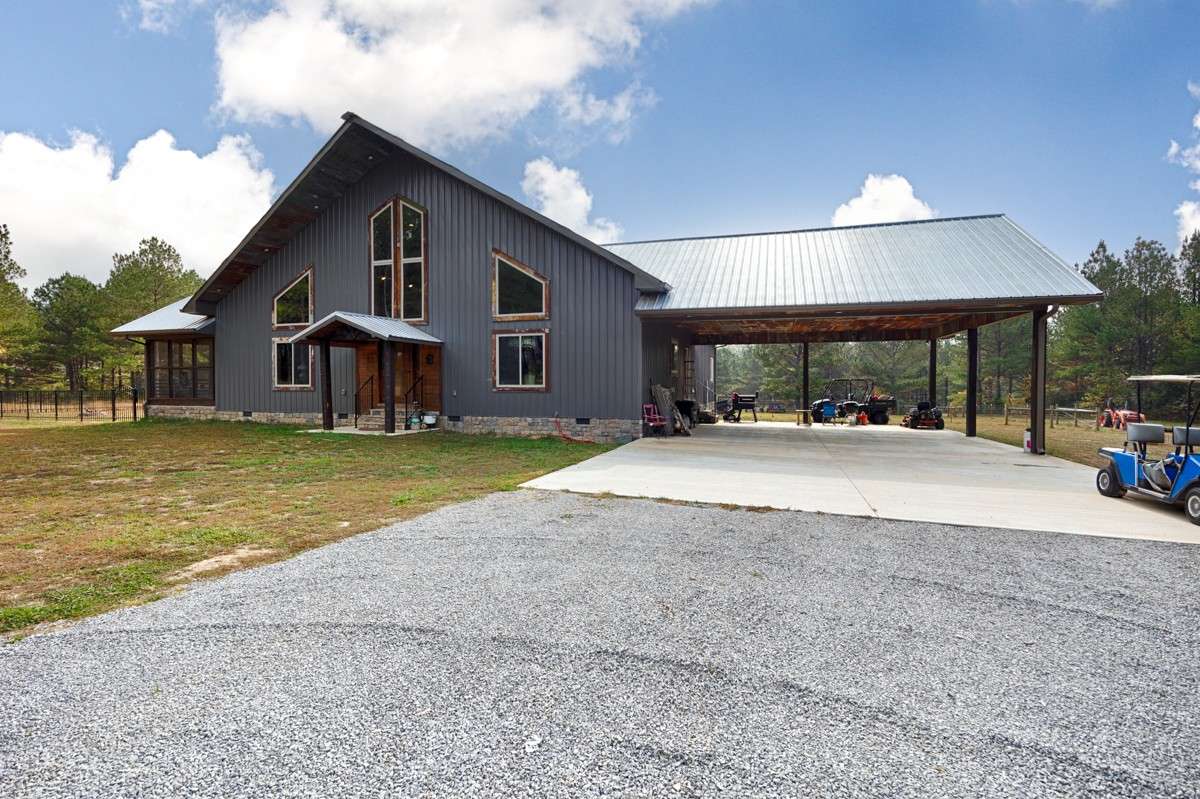 Front of house- gravel drive, concrete pad for parking and carport, metal building and roofing, large windows, covered front entry, screened porch