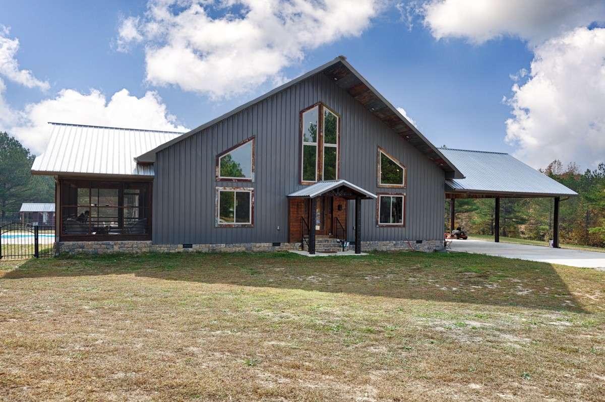 Front of house- gravel drive, concrete pad for parking and carport, metal building and roofing, large windows, covered front entry, screened porch
