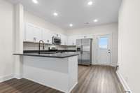 A fresh, modern kitchen featuring stainless steel appliances, white shaker cabinets, and a large peninsula with bar seating.