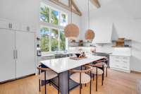 This angle highlights the seamless built-in refrigerator and oversized picture windows that flood the kitchen with natural light.