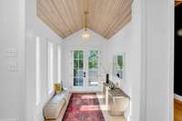 A bright, natural-light entry with tongue-and-groove wood ceilings and a bold chandelier—warm, welcoming, and unforgettable.