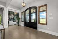 Elegant entryway with grand double doors, decorative glass, and scenic views. Polished concrete floors add a modern touch, while the adjacent library with built-ins enhances the inviting feel.