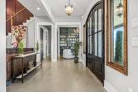 Elegant entryway with grand double doors, decorative glass, and scenic views. Polished concrete floors add a modern touch, while the adjacent library with built-ins enhances the inviting feel.