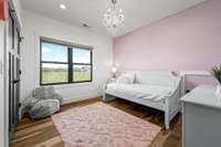 Bright & charming! This first of four upstairs bedrooms features a soft pastel accent wall, elegant chandelier, and large windows offering beautiful countryside views. A perfect retreat with plenty of natural light and cozy vibes.