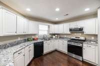 The bright, white kitchen is both stylish and efficient, featuring granite countertops, stainless steel appliances, a gas stove, and a spacious pantry for ample storage.