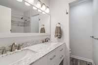 The bathroom features a double vanity, allowing multiple people to use the sinks simultaneously. Overhead vanity lighting enhances the space, adding both brightness and style.
