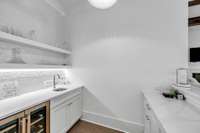Inside the wet bar room, a serving sink and beverage cooler and floating shelves make entertaining a breeze.