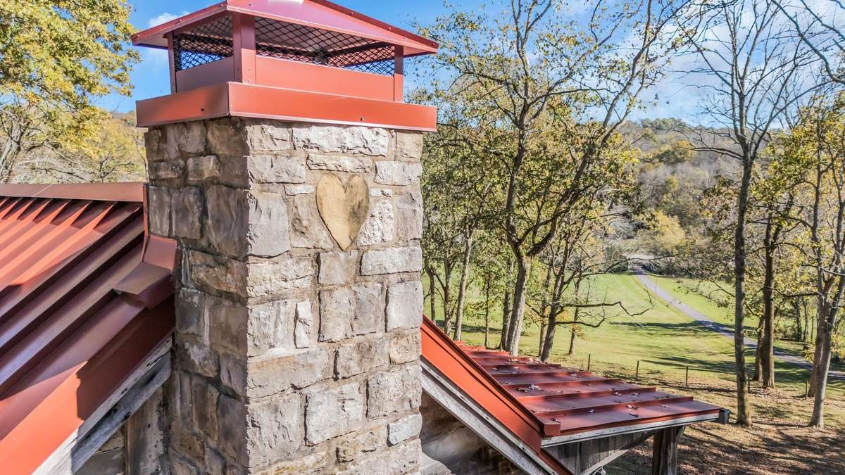 Braxton Dixson's signature stone heart is visible at the top of both chimneys. The roof is a new 24-gauge standing seam room with 4" of insulation under it. The chimney caps and gutters with leaf guards are all new.