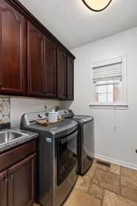 Laundry room featuring durable tile floors, an updated backsplash, and plenty of beautiful cabinetry—offering both style and ample storage for all your laundry needs!