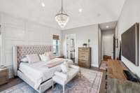 Hardwood flooring, crown molding, and a vaulted ceiling create a sense of warmth and grandeur, while an elegant chandelier and paneled accent wall add sophisticated charm