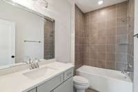 The ensuite bath features a large vanity with quartz countertops, tile flooring, and a tile-surround tub/shower combo, creating a comfortable and stylish space.