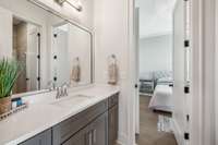 The guest bath is designed with elegance and functionality in mind, featuring tile flooring, a quartz vanity, and a walk-in shower with a tile surround and a frameless glass door.