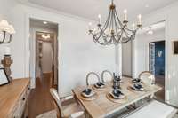 Elegant details include a candelabra chandelier, stylish sconces, rich hardwood flooring, and crown molding. Large windows with transoms invite natural light, adding warmth and sophistication to the space.