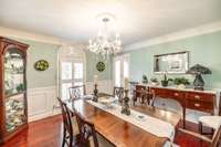 The formal dining room can be entered through the foyer hallway or from the kitchen.  Custom wall trim surrounds the room below the chair rail. Classic chandelier appoints this space perfectly.