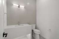 Lower floor powder room by the office with quartz apron vanity and tile wall. Mirror to be selected by the buyer.