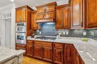 A gas cooktop with built-in hood, granite counters, and rich wood cabinetry give this kitchen both function and style. Subway tile backsplash and under-cabinet lighting add a clean, polished look.