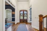 Rich wood double doors, tall ceilings, and detailed trim work create a welcoming entry filled with natural light and timeless style.