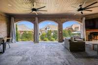The covered back patio offers a cozy outdoor retreat with a fireplace, mounted TV, and ceiling fans. Perfect for relaxing or entertaining year-round in comfort and style.