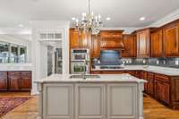 The kitchen features custom cabinetry, granite counters, double ovens, a large island with seating, and a foot-activated sweep suction for the central vacuum system. A deep walk-in pantry adds extra storage just steps from the main workspace.