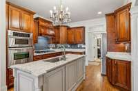 This chef's kitchen offers abundant cabinetry, granite counters, a gas cooktop, double ovens, and a custom island. Just beyond the fridge, access to the laundry room and garage keeps daily tasks convenient and connected.