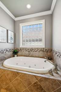 A deep whirlpool tub set beneath a glass block window offers the perfect place to soak and unwind, blending relaxation with privacy in the primary bath.