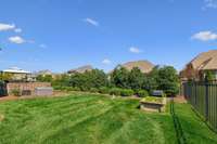 The backyard offers a lush green lawn with manicured landscaping and mature privacy hedges. There's even a built-in grill station, perfect for backyard BBQs or relaxing evenings under the stars.