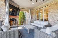 The covered back porch features a cozy fireplace, mounted TV, and plenty of space for lounging or entertaining. It's a perfect spot to relax year-round and enjoy the outdoors in comfort and style.