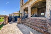 Another view of the back patio shows the beautiful brick staircase leading up to the arched, covered area with dual ceiling fans. Just below is a dedicated grilling zone with space for multiple cookers and a shaded prep area.