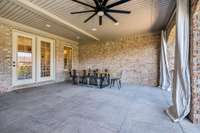 This expansive covered patio has room for both lounging and dining. Features include a ceiling fan, custom curtains, and ample space to relax or entertain in comfort. A perfect spot to enjoy the outdoors with shade and privacy.