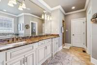 The primary bath features dual vanities with rich marble counters, custom cabinetry, and a large mirror. Thoughtful design and finishes create a refined space to start and end your day.
