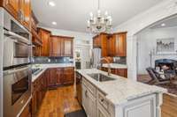 This kitchen combines beauty and function with warm wood cabinetry, a gas cooktop, double ovens, and granite countertops. The open layout connects to the living room, ideal for entertaining or daily living.