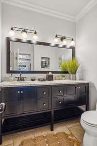 This main-level half bath features a wide granite vanity with rich cabinetry, modern lighting, and ample storage. It's conveniently located for guests and everyday use.