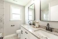 Newly renovated bathroom with double sinks, granite, and tile.