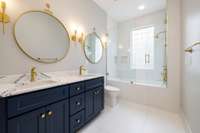 A tastefully renovated Jack-and-Jill bathroom seamlessly connects this bedroom to the next. The space boasts new tile flooring, sleek cabinetry, Kohler faucets, stylish lighting, and a luxurious tub with artfully installed tile surround.