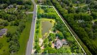 A bird's eye view of this sprawling lot with a private pond and mature landscaping. A long driveway leads to the home, offering both privacy and stately curb appeal.