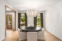 The formal dining space blends clean simplicity with a sculptural chandelier and verdant window views.