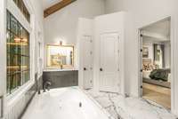 Vaulted ceilings with wood beams add height and texture to this primary bathroom, complete with soaking tub positioned between large windows.