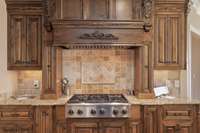This cooking space is surrounded by stained wood cabinets included pull out spice racks and stunning range hood.