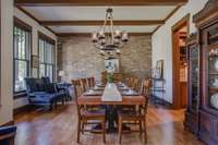 The expansive dining room features a charming brick wall facade, wood beams, & motorized screens, all overlooking the front lawn. It comfortably accommodates more than 24 guests.