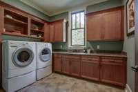 The spacious laundry room has extensive cabinetry, a sink, and granite countertops.