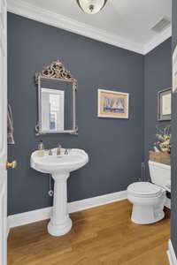 Powder room has a pedestal sink and hardwood floors and is situated away from the living areas.