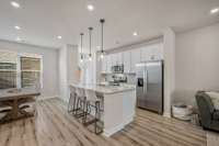 The kitchen features granite countertops, white painted cabinets, stainless steel appliances, and a large island. The island has countertop seating for three as well as three pendant lights.