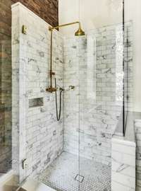 Marble countertops and Calacatta shower with frameless surround and brass fixtures.