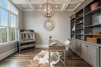 The well-appointed office features a wall of built-ins, a coffered ceiling and glass french doors