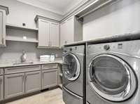 Fully equipped laundry room with front loading washer & dryer, utility sink, and plenty of cabinets for storage