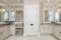 The expansive spa-like bathroom features separate extended vanities including a make-up counter, trimmed mirrors surrounding the perimeter, and marble tile floors