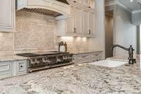 Gorgeous blend of granite counters and subway tile backsplash with an artistic design highlights the range wall