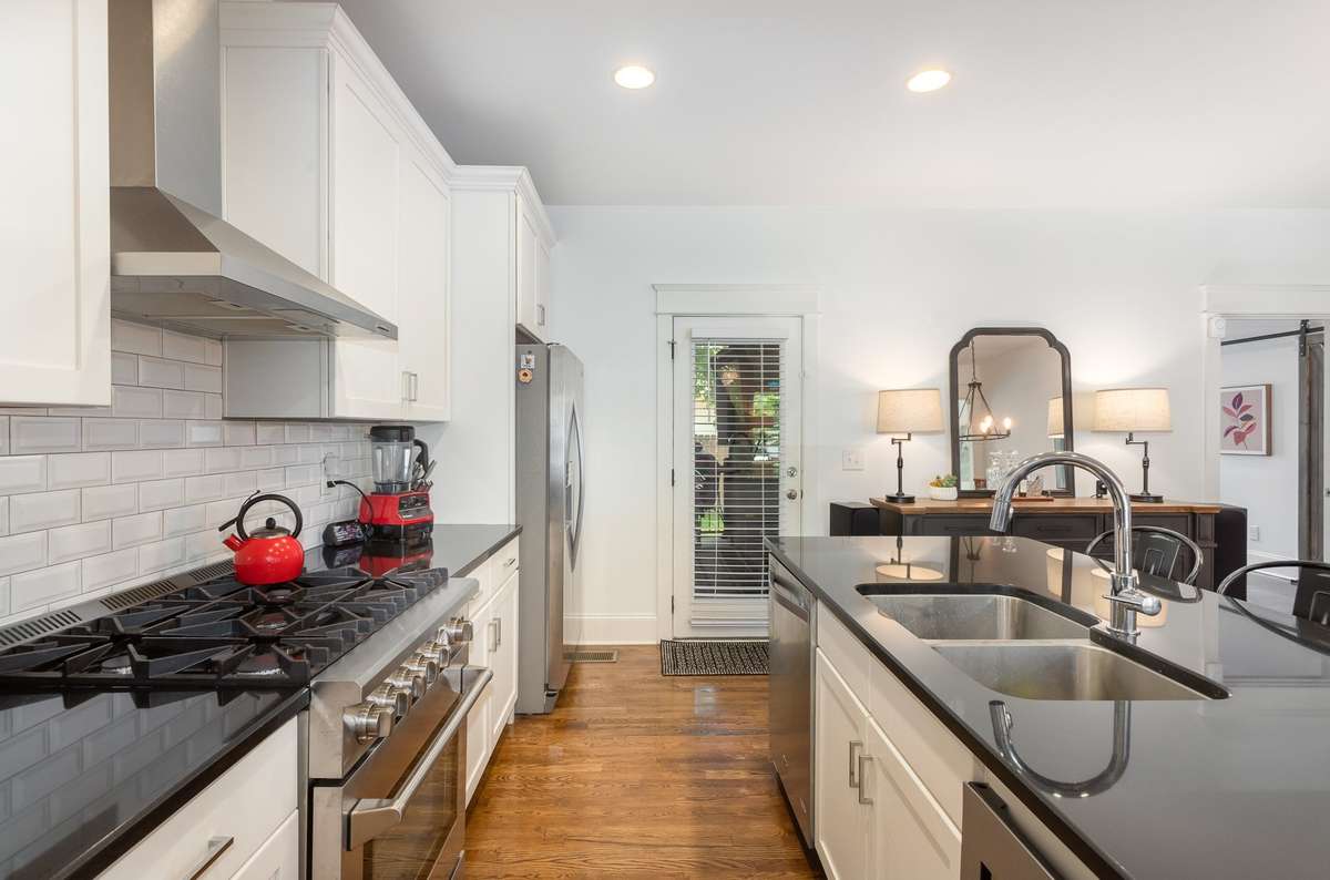 The kitchen features a large island with a sink and bar seating, a tile backsplash, and a gas range. Open to the dining area with direct access outside, to the screened-in porch and backyard.